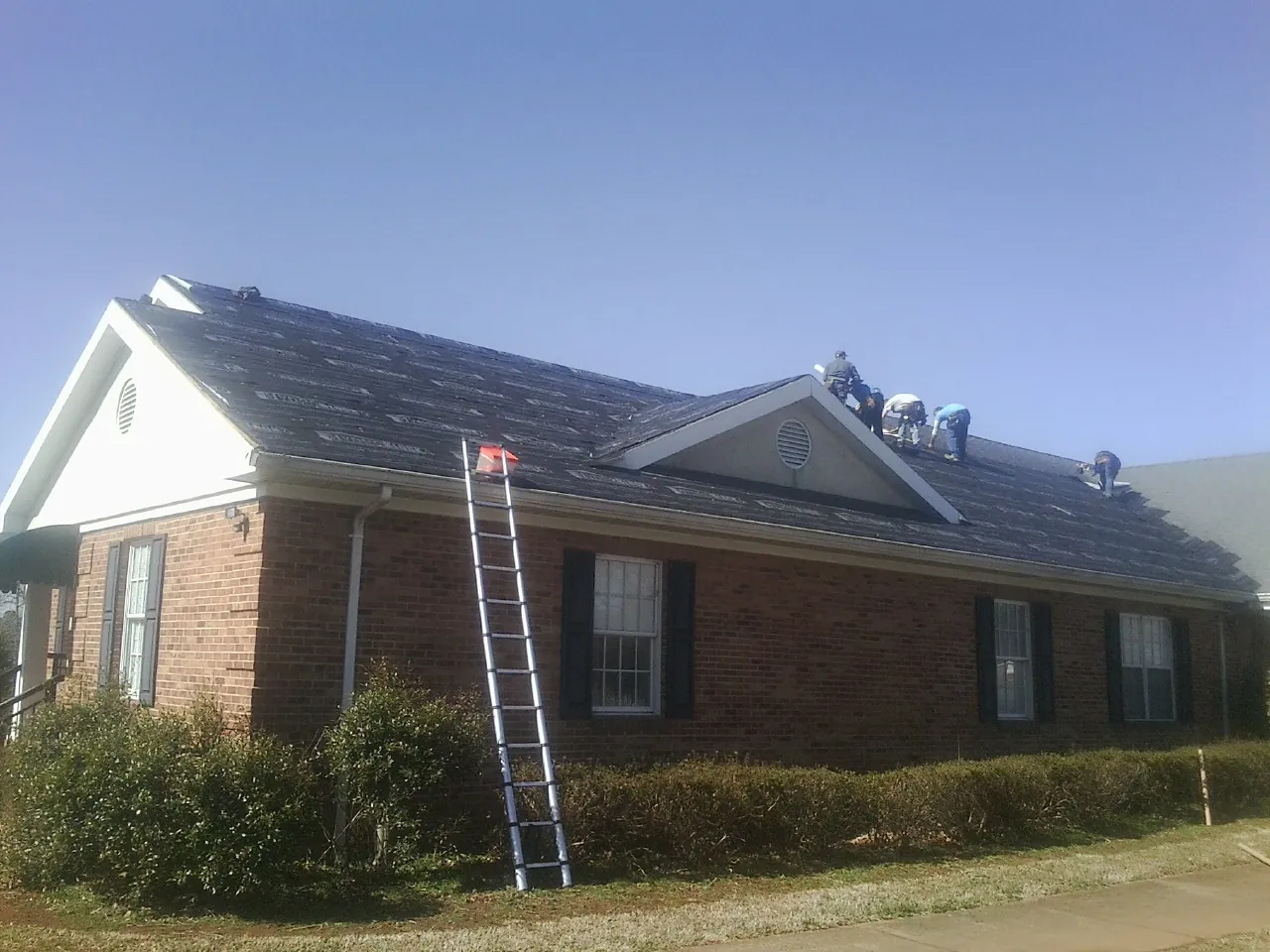 Crew tearing shingles off a brick ranch roof with a ladder set — Emergency Roof Repair work by our crew in Columbiana
