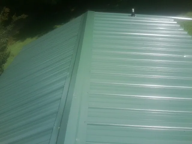 New green metal panels meeting at the ridge of a roof — Flat Roof Repair work by our crew in Columbiana