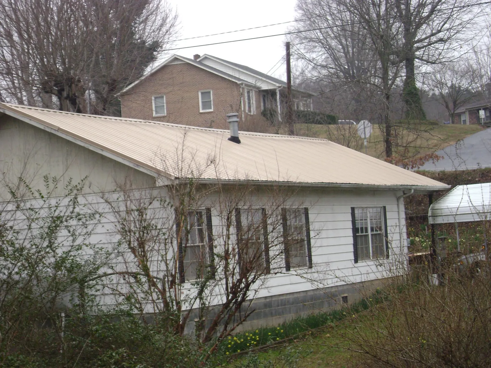 Tan metal roof on a white sided house set into a hillside — Commercial Roofing by Roofing Brothers in Columbiana