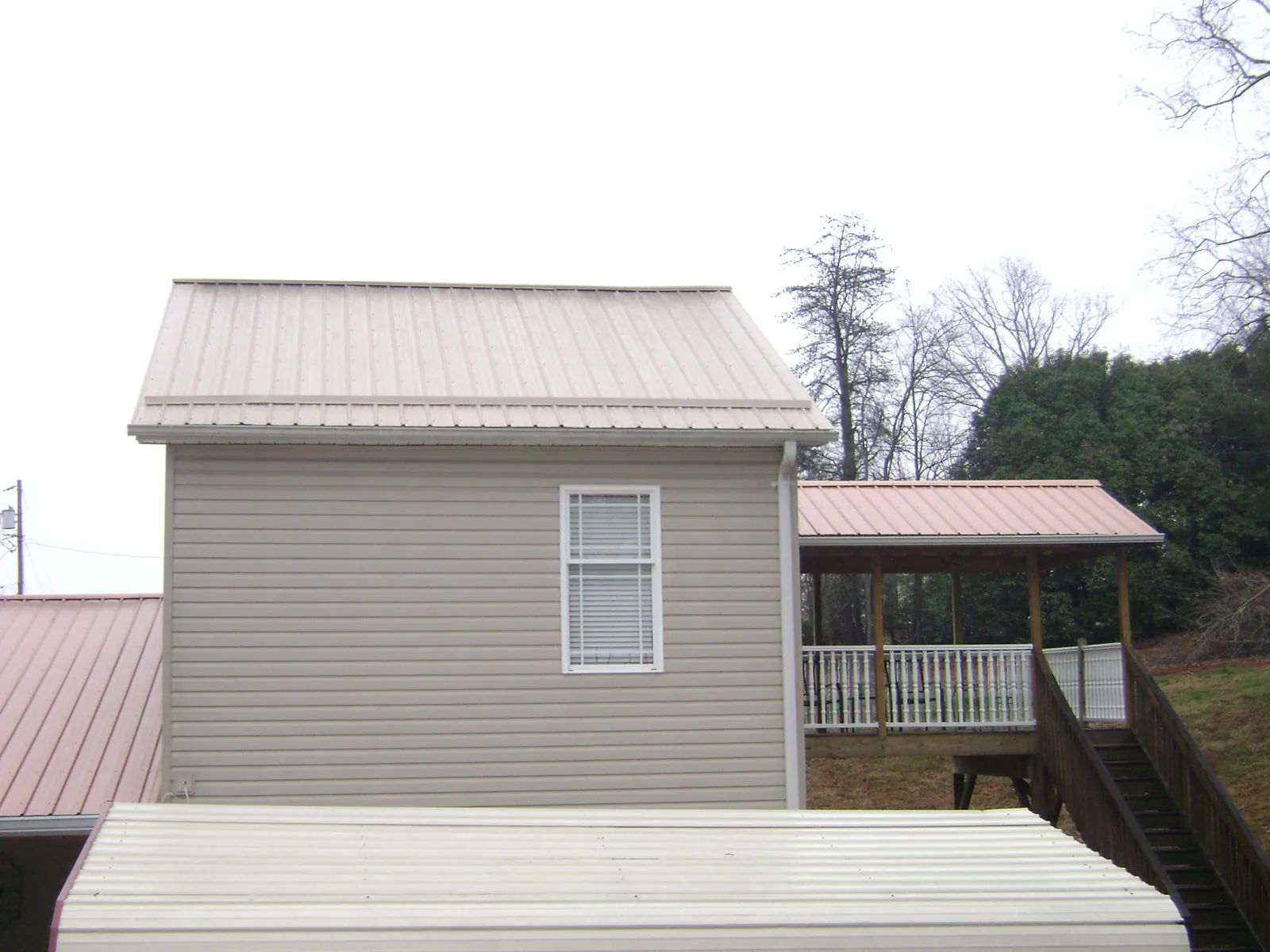 Tan metal roofs on a two story addition and attached porch, from a Roof Replacement job in Columbiana